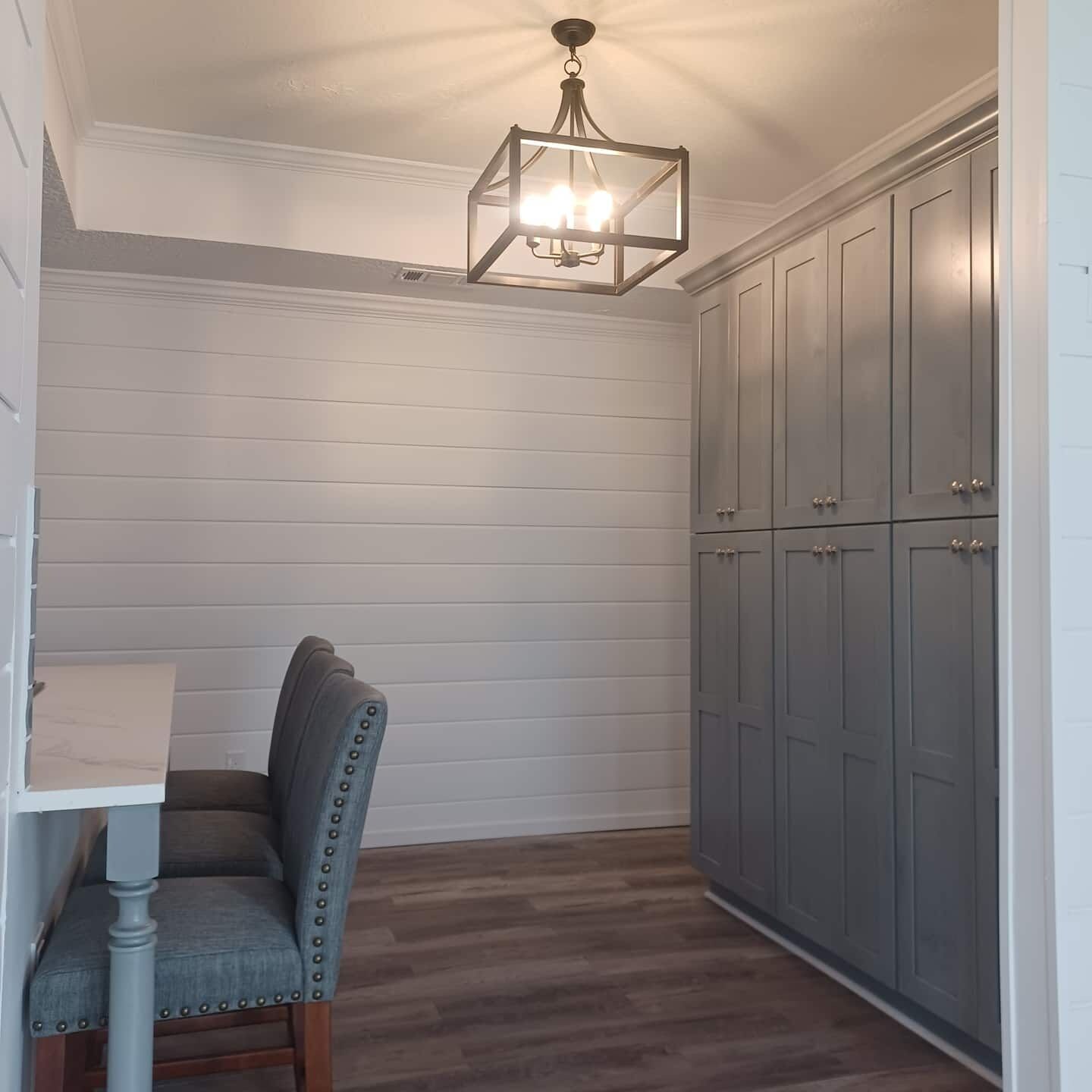 A room with a wooden floor, a chair, a cabinet, and a hanging light fixture.