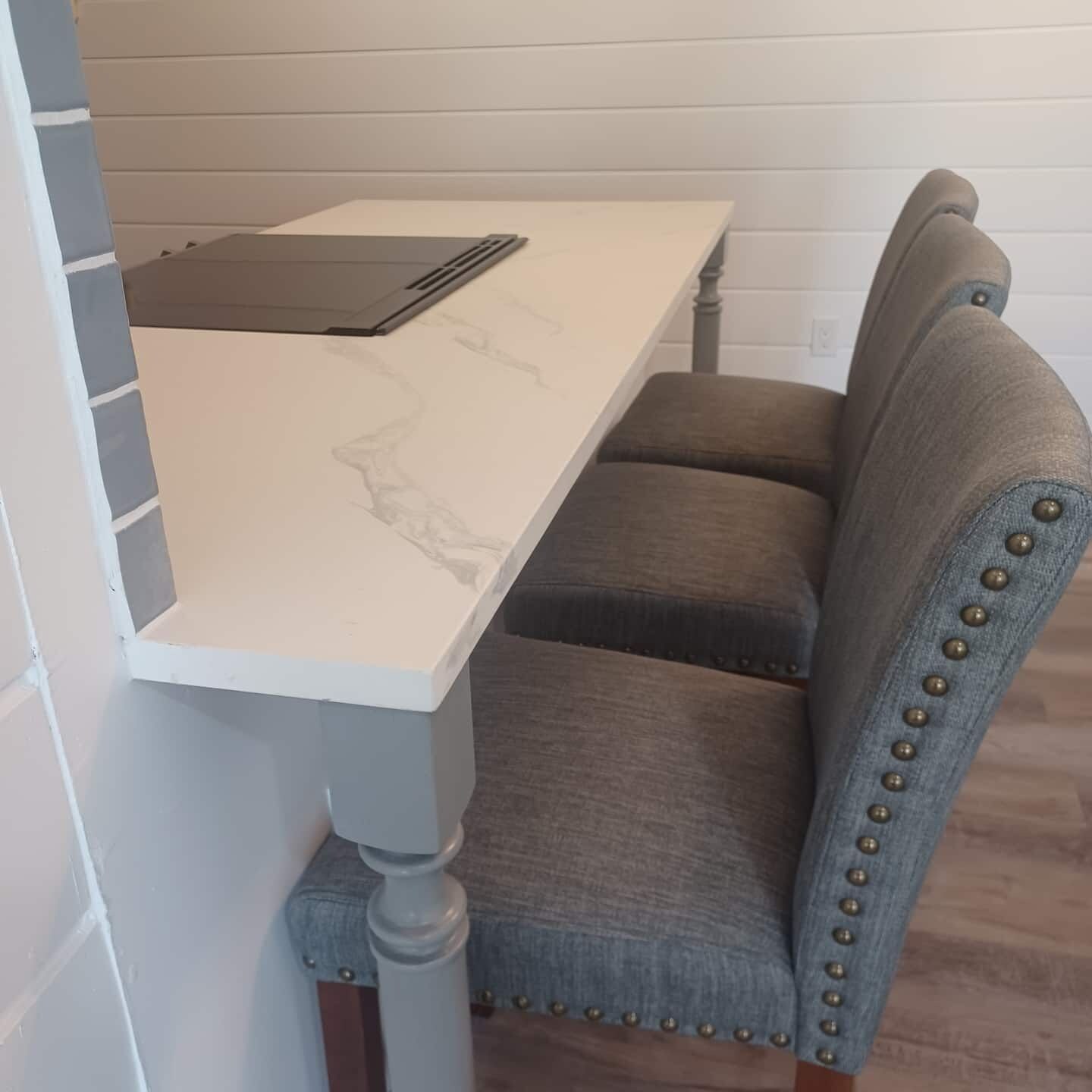 A dining area with a marble table, two upholstered chairs, and a wooden chair with metal studs.
