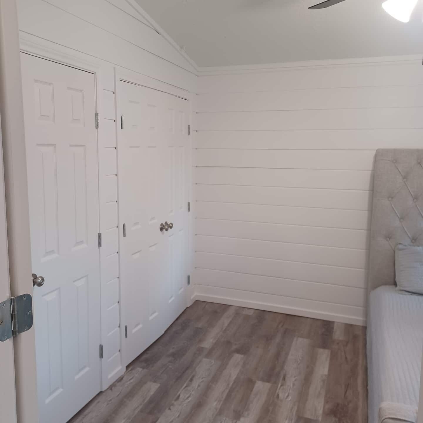 Een kamer met een witte deur, een gestoffeerd hoofdeinde en een houten vloer.