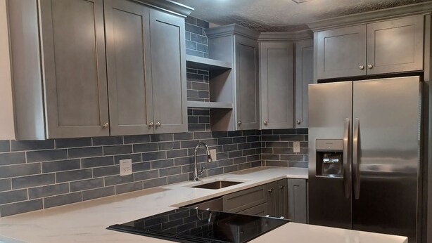 Une cuisine moderne avec des meubles gris, un réfrigérateur en acier inoxydable et une plaque de cuisson noire.