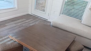 Un espace repas avec une table en bois et des bancs assortis, un sol recouvert de moquette et un mur blanc agrémenté d’une fenêtre.