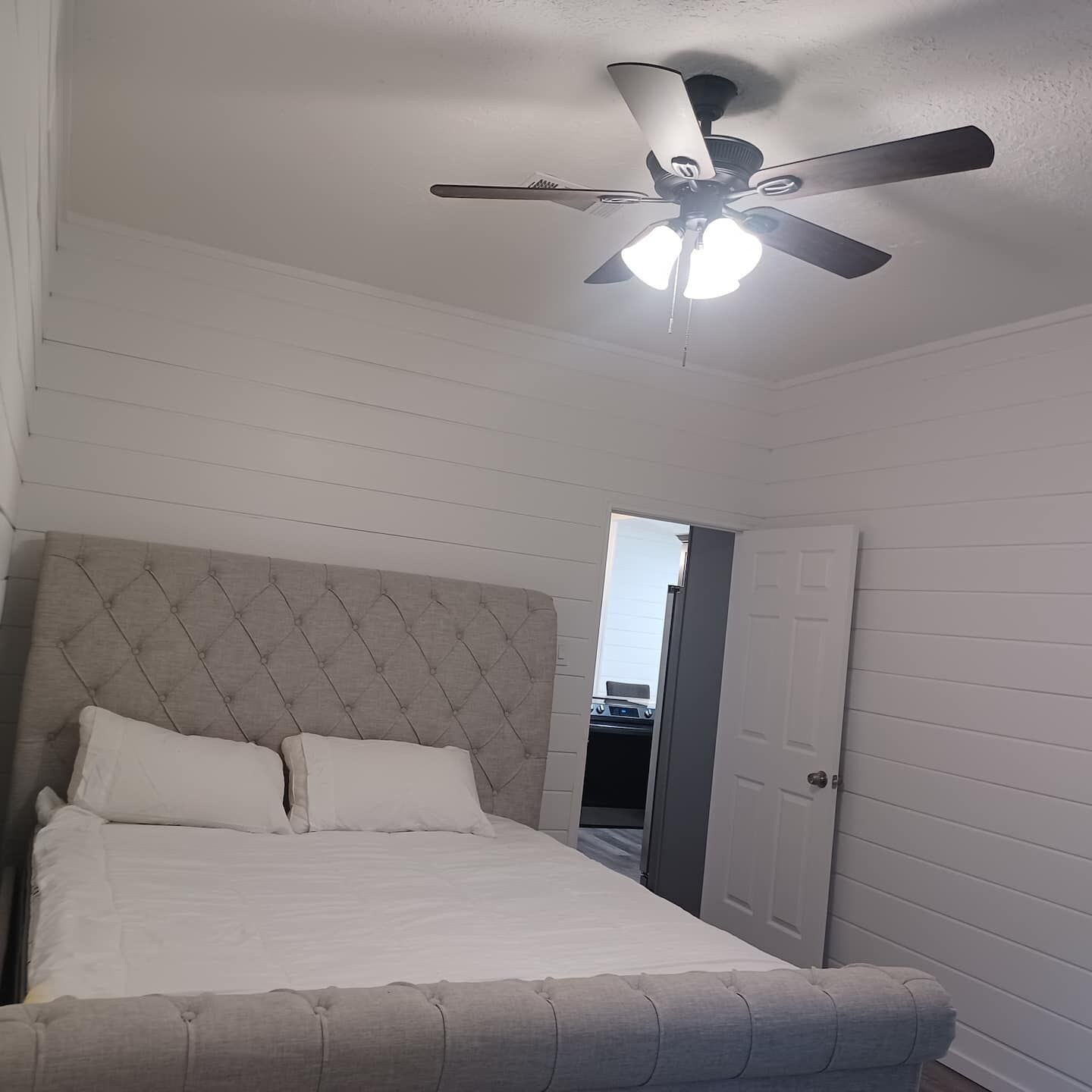 Een slaapkamer met een bed, een plafondventilator en een deur naar een andere kamer.