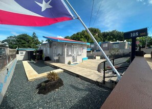 A building with a flagpole, a sign reading "108", and a small structure with a red roof. - Casa Qodesh #2: Oasis Eco-Gem, Solar & Water (Arecibo)
