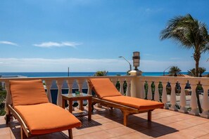 A balcony with two lounge chairs and a small table, overlooking a coastal view. - Steps from the beach • Ocean view villa (Noord)