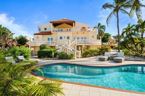 A two-story building with a swimming pool, outdoor seating, and palm trees. - Steps from the beach • Ocean view villa (Noord)