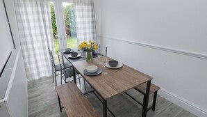 A dining area with a wooden table, chairs, and a bench. There is a view of greenery outside through the window. - Maes Hyfryd (Clynderwen)