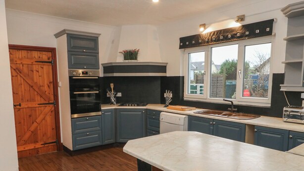 A kitchen with blue cabinets, a wooden door, a stove, and a window with a view. - Maes Hyfryd (Clynderwen)