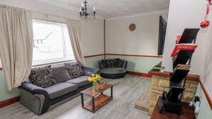A living room with a grey sofa, a coffee table with a vase of flowers, a fireplace, and a bookshelf with books. - Maes Hyfryd (Clynderwen)