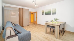 A modern living room with a sofa, a dining table with chairs, and a wooden floor. There is a sliding door and a door leading to another room. - Kraków Huculska Apt — Balcony, Workspace (Kraków)