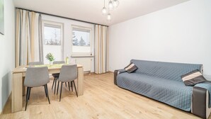 A modern living room with a sofa, a dining table with chairs, and a window with curtains. - Kraków Huculska Apt — Balcony, Workspace (Kraków)