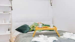 A neatly arranged bedroom with a bed, a bedside table with a plant, and a shelf with books and a lamp. - Kraków Huculska Apt — Balcony, Workspace (Kraków)