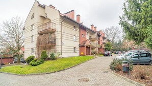 A multi-story residential building with a brick facade, a small garden area, and a paved driveway. - Kraków Huculska Apt — Balcony, Workspace (Kraków)