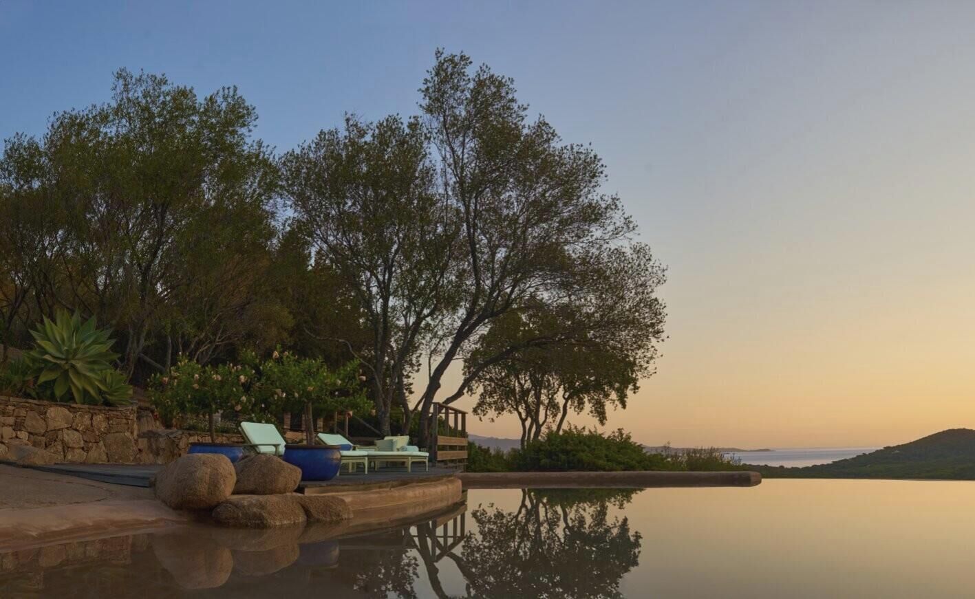A serene outdoor area with a pool, lounge chairs, and a stone wall.
