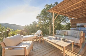 Una terraza de madera con mobiliario exterior, una parrilla y vistas del paisaje.