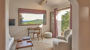 Een kamer met uitzicht op een groen landschap, een houten bureau, een stoel, een bank en een groot raam met gordijnen.