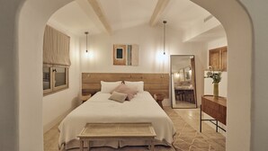 Een slaapkamer met een groot bed, een houten hoofdeinde, een nachtkastje, een bankje, een spiegel en uitzicht op de badkamer.