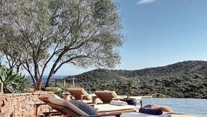 Een houten terras met lounge stoelen en een rieten mandje, met uitzicht op een waterpartij en een glooiend landschap.