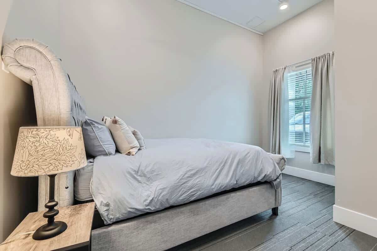 A bedroom with a bed, a nightstand with a lamp, and a window with curtains.