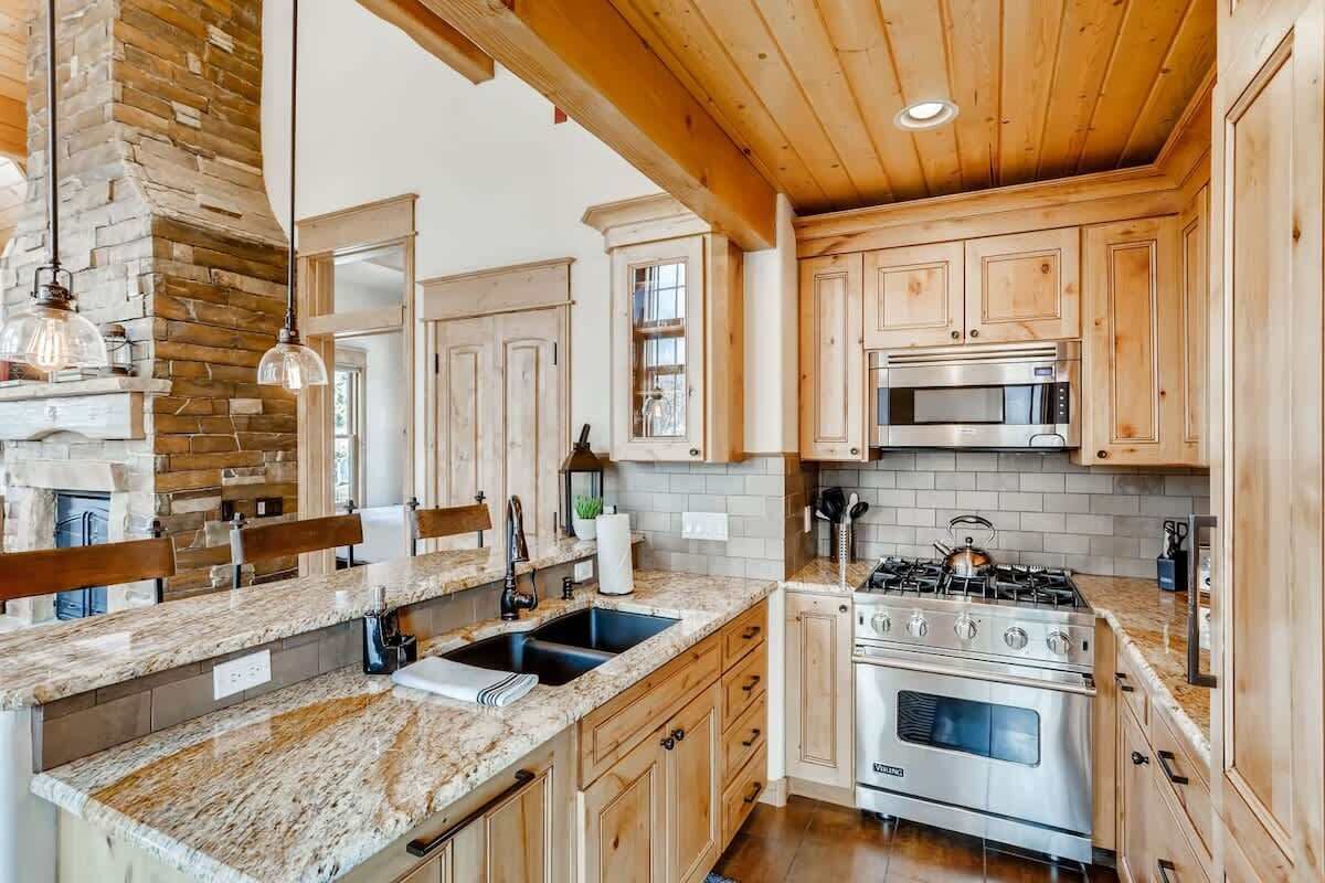 Una cocina con armarios de madera, encimeras de granito, estufa integrada y pared de piedra.