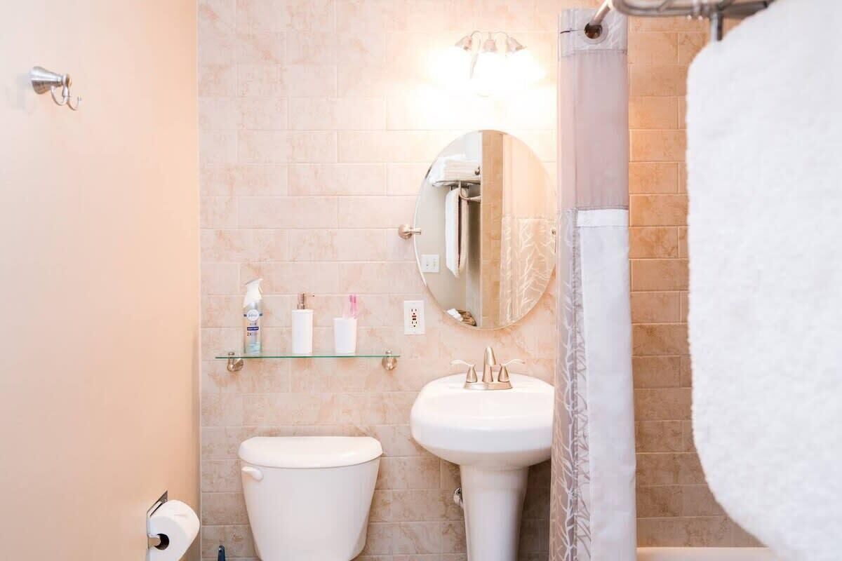 A bathroom with a toilet, sink, and mirror. There is a glass shelf with toiletries.