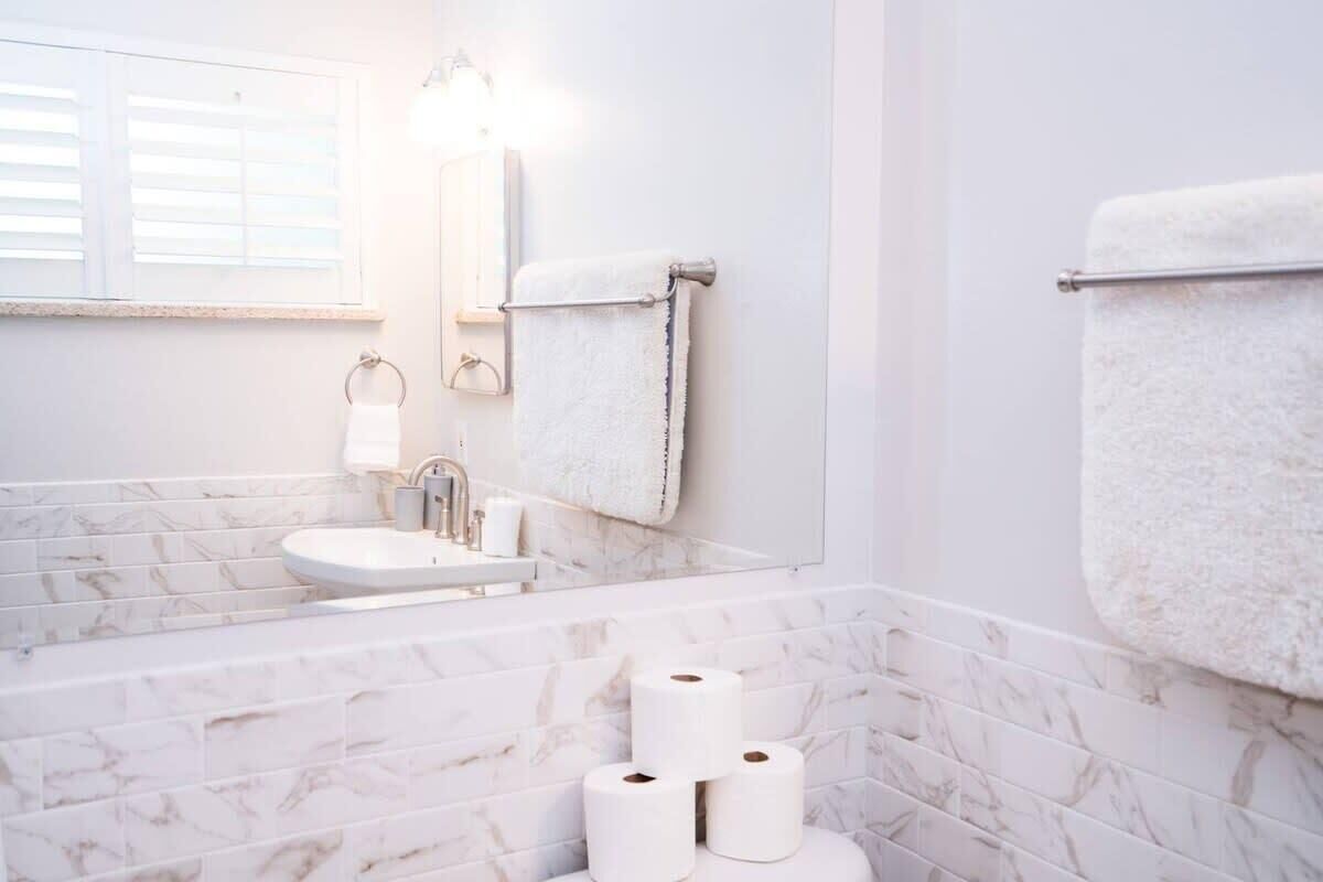 A bathroom with a marble-tiled wall, a sink, a mirror, and three rolls of toilet paper on a holder.