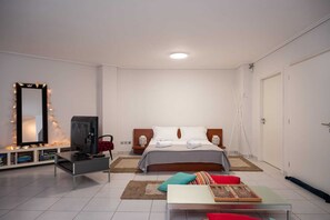 Ein modernes Schlafzimmer mit einem Bett, Nachttischlampen, einem Fernseher, einem Spiegel und einem kleinen Tisch mit Büchern.