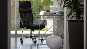 Moderni toimistotila, jossa on musta toimistotuoli, lasinen työpöytä ja ruukussa oleva kasvi.