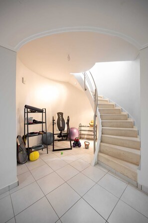 Eine Treppe führt zu einer Zwischenebene mit Trainingsgeräten und einem Regal.