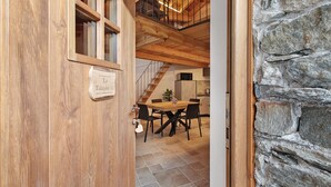 A wooden door with a sign, a dining area with a table and chairs, and a stone wall.