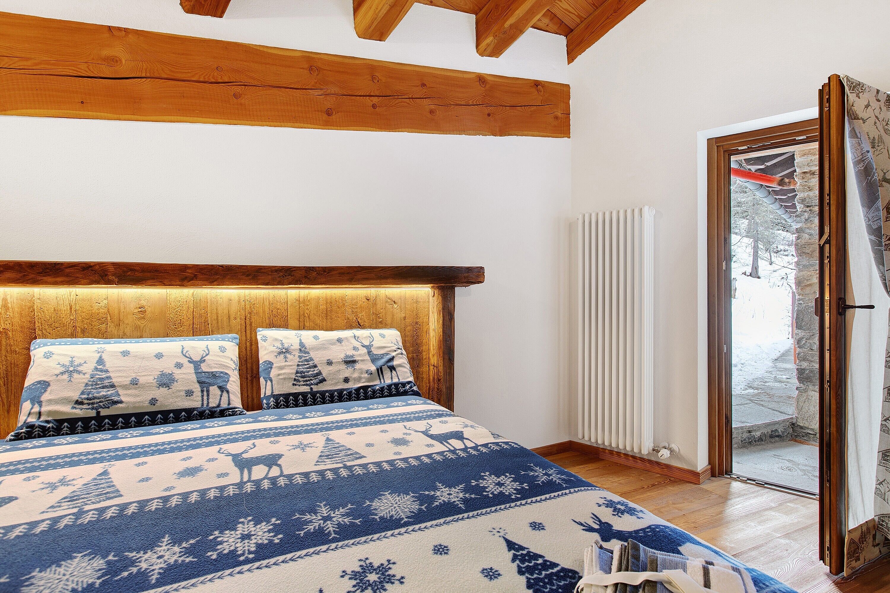 Camera da letto con testiera in legno, un letto con copriletto a motivi blu e bianchi e vista su una zona esterna innevata attraverso una porta in vetro.