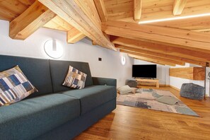 A cozy living room with a sofa, pillows, a flat-screen TV, wooden beams, and a round window.