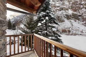 A wooden balcony with a stone wall, overlooking a snow-covered mountain landscape.