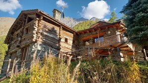 A rustic log cabin with a stone foundation, a balcony, and a mountain backdrop.