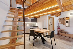 A modern kitchen with a wooden staircase, a dining area with a table and chairs, and a fire extinguisher on the wall.