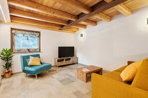 Un salon avec un plafond en bois, un téléviseur posé sur un meuble en bois et deux canapés.