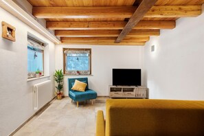 Une pièce avec un plafond en bois, un fauteuil bleu, un canapé jaune, une télévision et une fenêtre donnant sur un paysage agréable.