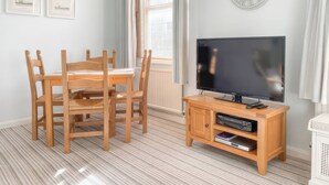 A room with a wooden dining table, four chairs, a television on a wooden stand, and a clock on the wall. - Snugglers Cove (Dartmouth)