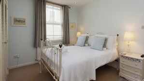 A bedroom with a bed, bedside lamps, a dresser, and a window with curtains. - Snugglers Cove (Dartmouth)