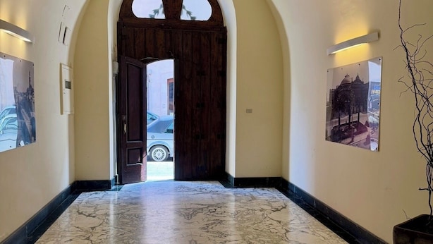 Un pasillo con suelo de mármol, un arco de entrada y cuadros en las paredes.
