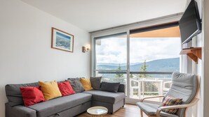 Un salon moderne avec un canapé d’angle gris, une table basse en bois et un fauteuil avec un coussin.