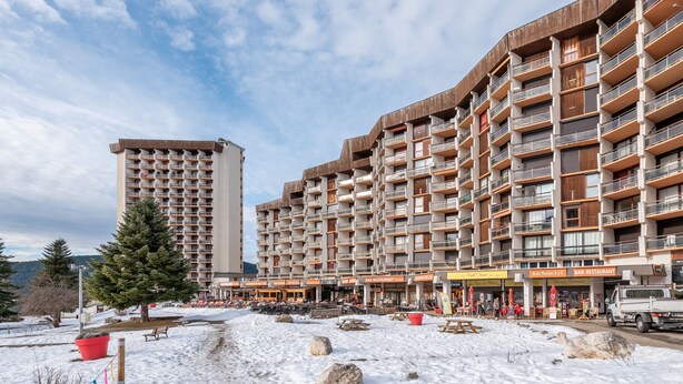 Un immeuble à plusieurs étages doté de balcons, dont le sol est recouvert de neige, et qui propose des espaces de détente en plein air.