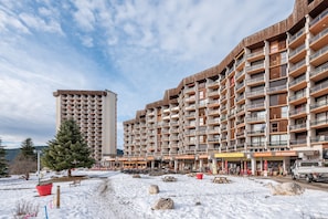 Un edificio de varios pisos con balcones, suelo cubierto de nieve y zonas de estar al aire libre.