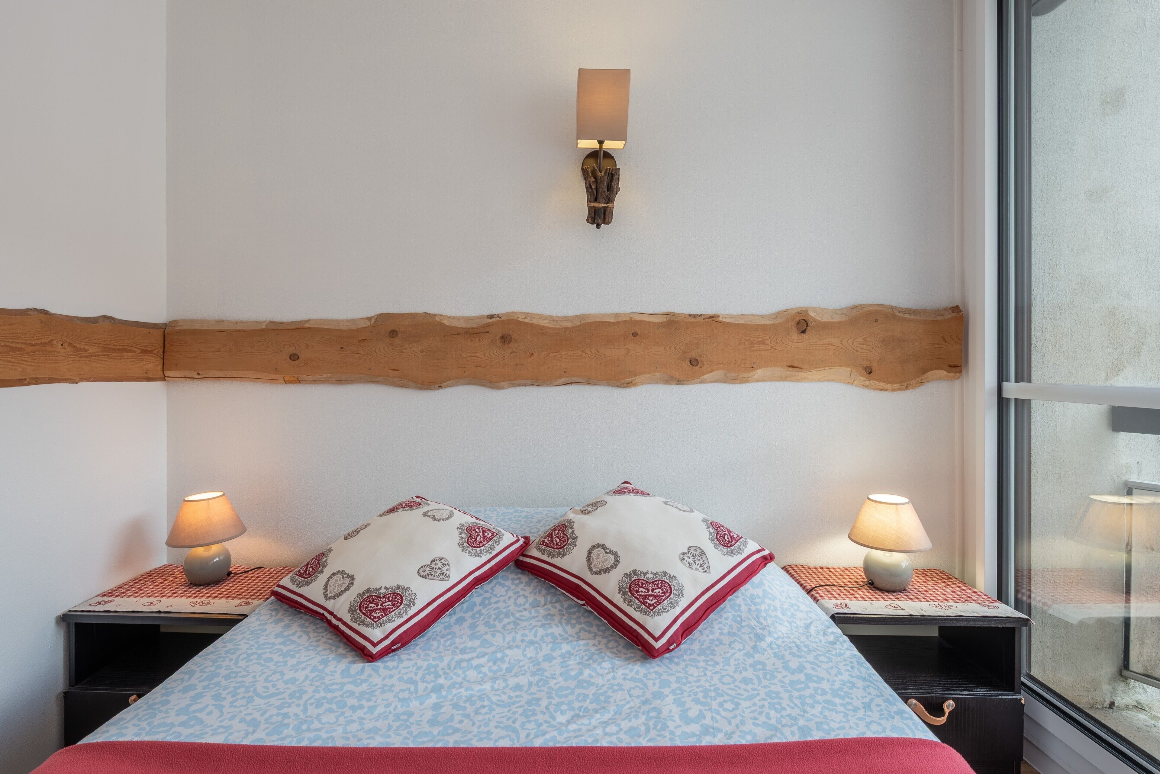 A bed with patterned pillows, bedside lamps, a wooden headboard, and a window with a view.