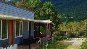 Une maison dotée d’un porche et d’une cour clôturée, entourée de verdure et de collines.
