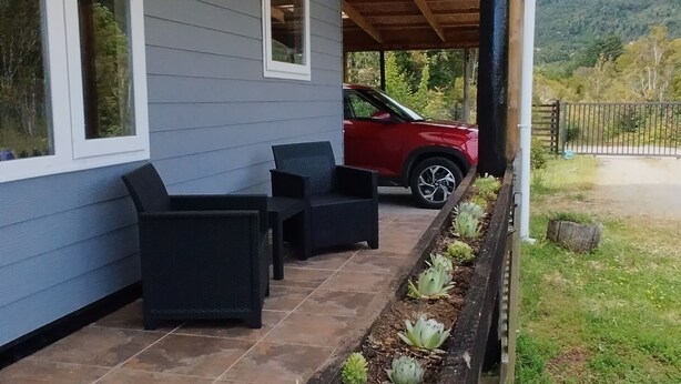 Un patio couvert avec des sièges d’extérieur, un véhicule et un parterre de fleurs.