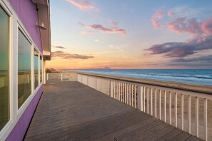 Una terraza de madera con baranda blanca que da a una playa al atardecer.