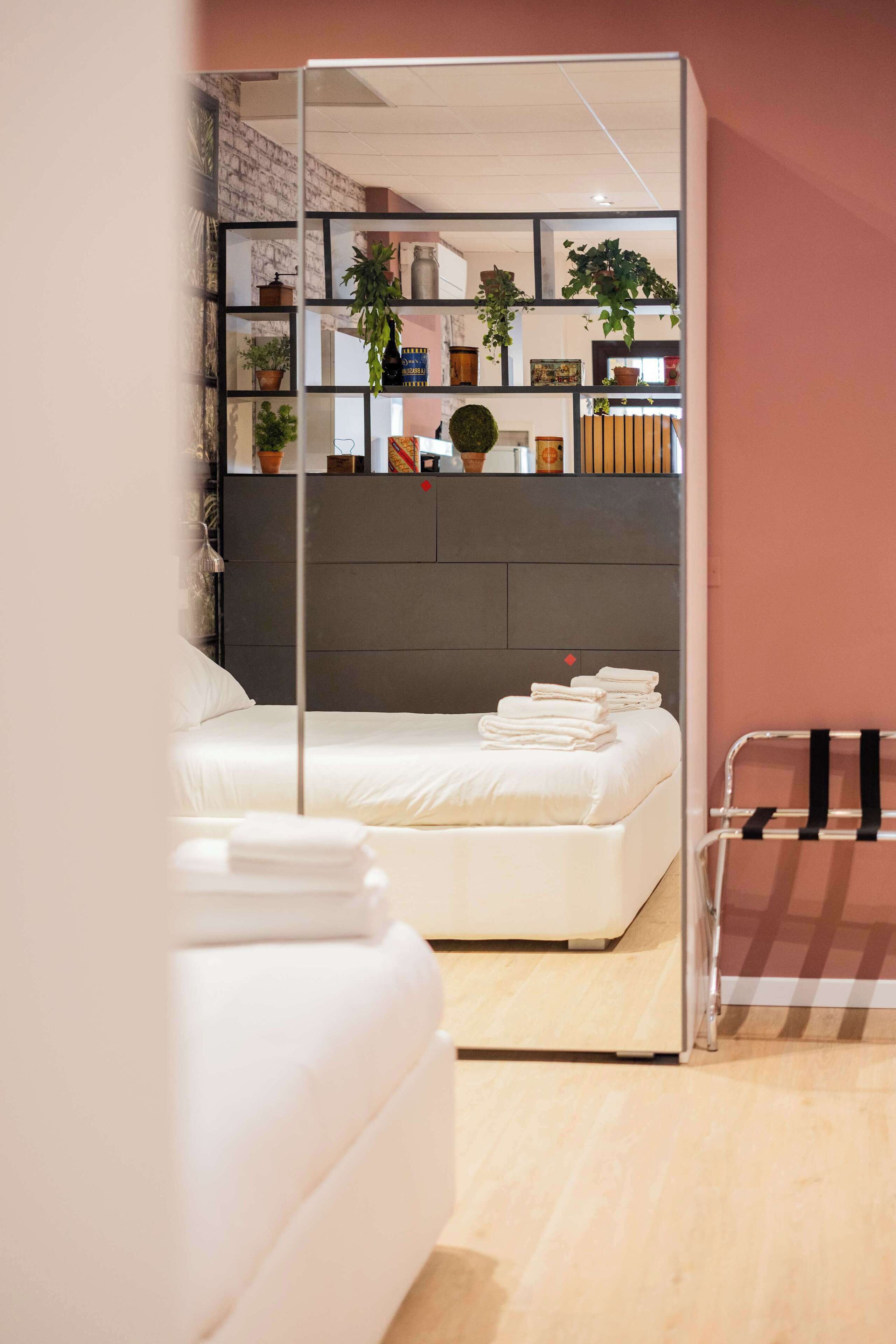 Une chambre à coucher moderne comprenant un lit, une table de chevet, un miroir et une étagère avec des plantes et des objets décoratifs.