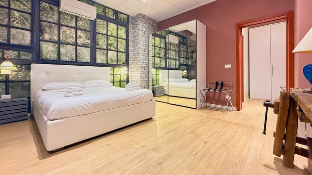 Une chambre avec un grand lit, un plancher en bois et une vue sur l’extérieur, visible à travers une porte vitrée.