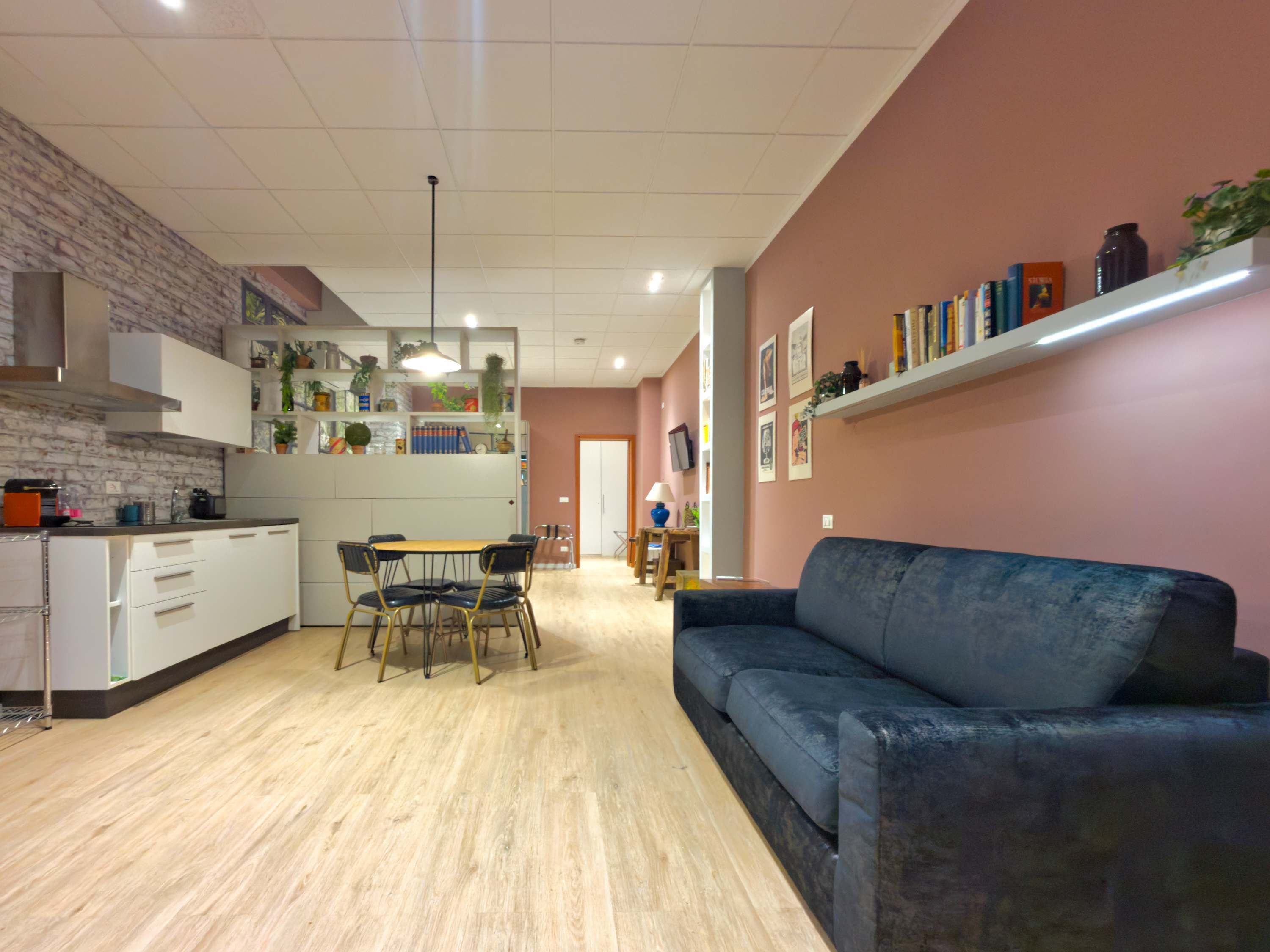 A modern kitchen with a dining area, a sofa, and a bookshelf.