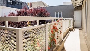 Un pasillo estrecho con una cerca blanca, plantas rojas florecientes y una puerta al final.
